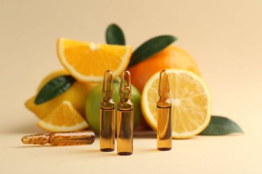 Cilt bakımı ampulleri C vitamini, farklı turunçgil meyveleri ve bej arka planda yapraklar
