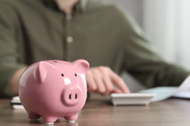 Finansal tasarruflar. Ahşap masada hesap makinesi kullanan adam, domuz kumbarasına odaklan.