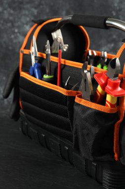 Farklı pense, ingiliz anahtarı ve siyah masada tamir için diğer aletlere sahip çanta, yakın plan.