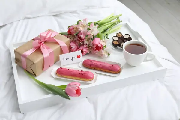 Tasty breakfast served in bed. Delicious desserts, tea, flowers, gift box and card with phrase I Love You on tray
