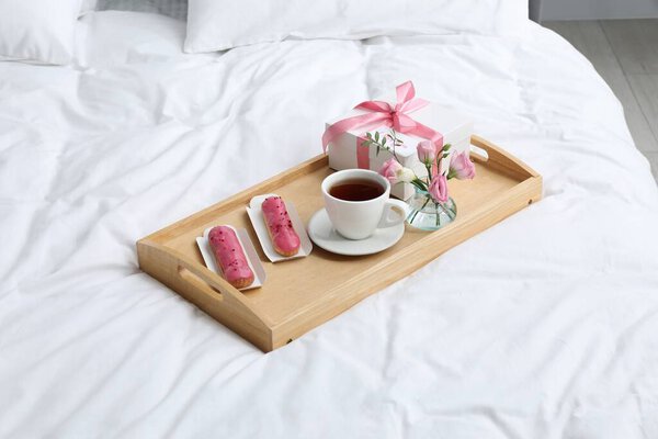 Вкусный завтрак подается в постель. Вкусные эклеры, чай, подарочная коробка, цветы и открытка с фразой I Love You on tray