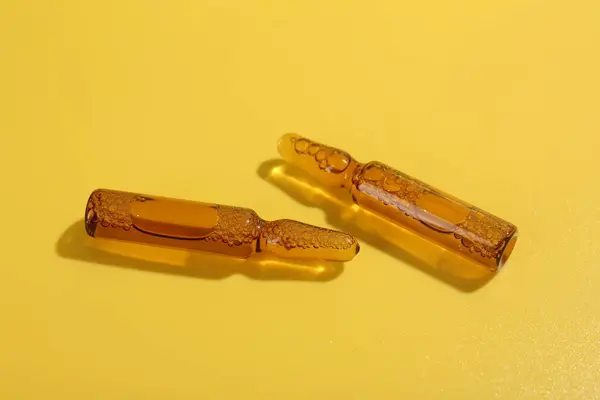 Glass ampoules with liquid on yellow background, closeup
