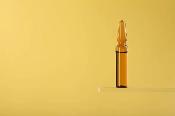 Glass ampoule with liquid on yellow background. Space for text