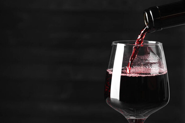 Pouring red wine into glass against dark background, closeup. Space for text