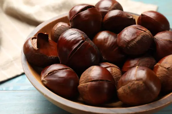stock image Fresh edible sweet chestnuts in bowl on light blue wooden table, closeup
