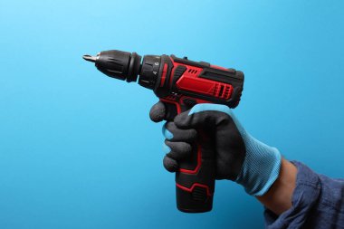 Açık mavi arka planda elektrikli tornavida tutan tamirci, yakın plan.