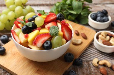 Lezzetli meyve salatası kasede ve ahşap masada malzemeler, yakın plan.