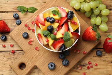 Lezzetli meyve salatası kasede ve ahşap masada malzemeler var.