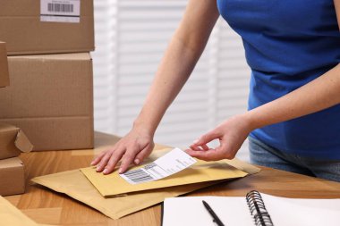 Paketleme. Postane çalışanı, kapalı bir masadaki çantaya barkod yapıştırıyor.