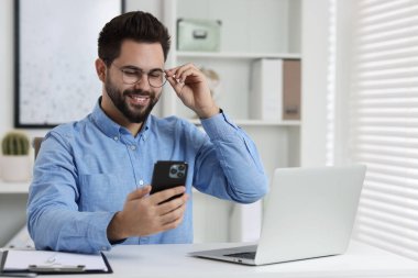 Ofisteki beyaz masada akıllı telefon kullanan mutlu genç adam.