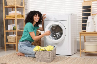 Çamaşır makinesinin yanında çamaşırları olan mutlu kadın.