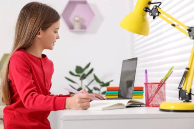 E-öğrenme. İçerideki masada online ders sırasında not alan tatlı kız.