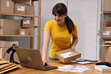 Paketleme. İçerideki ahşap masada dizüstü bilgisayar kullanan bir postane çalışanı.