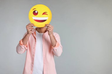 Gri arka planda mutlu bir göz kırpma ifadesiyle yüzünü kapatan adam. Metin için boşluk