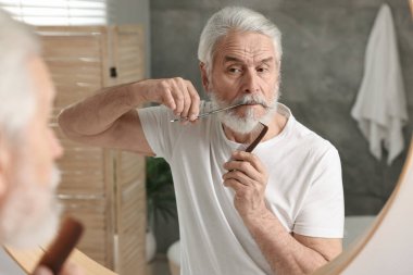 Banyoda aynanın yanında makasıyla bıyık buduyor.