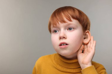 Gri arka planda işitme cihazı olan küçük çocuk, mesaj için boşluk