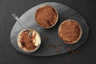 Bardakta nefis tiramisu, siyah masada kaşık ve kahve çekirdekleri.