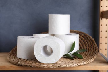 Tuvalet kağıdı ruloları ve ahşap rafta yeşil yapraklar.