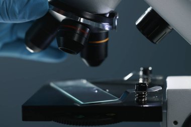 Karanlık arka planda mikroskopla çalışan bilim adamı, yakın plan