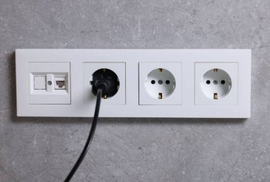 Gri duvarda elektrik prizi ve prizler var.