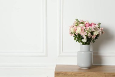 Beyaz duvarın yanındaki ahşap masada vazoda duran güzel bir çiçek buketi.