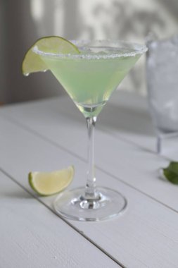 Lezzetli Margarita kokteyli beyaz ahşap masada limon ve cam.