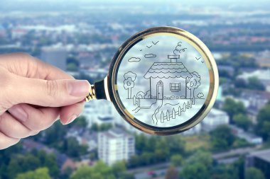 Kadın elinde büyüteçle şehre karşı bir ev çiziyor, yakın plan. Apartman ara