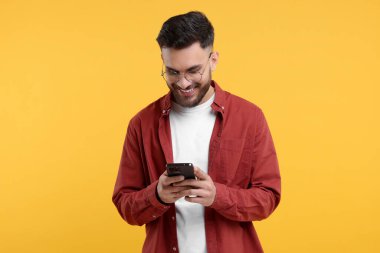 Sarı arka planda akıllı telefon kullanan mutlu genç adam.