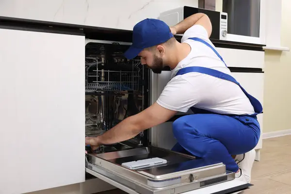 Serviceman repairing and examining dishwasher in kitchen
