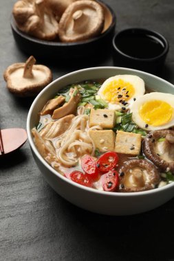 Erişte çorbası. Bir kase lezzetli ramen ve malzemeler siyah masada, yakın plan.