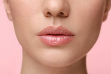 Pembe arka planda dudak parlatıcısı takan güzel bir kadın. Yakın plan.
