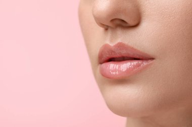 Pembe arka planda dudak parlatıcısı takan güzel bir kadın, yakın plan. Metin için boşluk