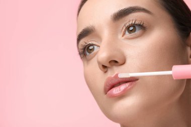 Pembe arka planda dudak parlatıcısı uygulayan kadın, metin için boşluk