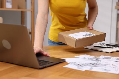 Paketleme. Kapalı alanda, ahşap masada dizüstü bilgisayar kullanarak posta memuru.