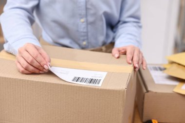 Paketleme. Postane çalışanı kapalı bir kutuya barkod yapıştırıyor.