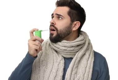Beyaz arka planda boğaz spreyi kullanan fularlı genç bir adam.