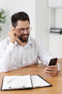 Ofisteki ahşap masada akıllı telefon kullanan yakışıklı genç adam.