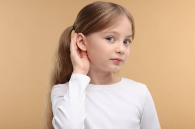 Soluk kahverengi arka planda işitme sorunu olan küçük bir kız.