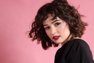 Pembe arka planda dalgalı saç stili olan güzel bir genç kadının portresi. Metin için boşluk