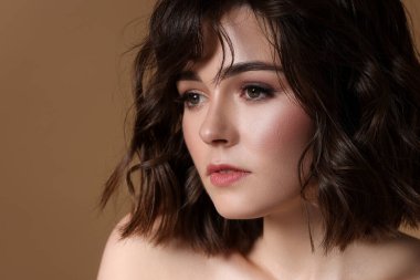 Kahverengi arka planda dalgalı saç stili olan güzel bir genç kadın. Metin için boşluk