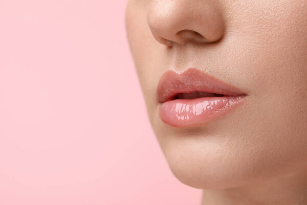 Женщина с красивым блеском для губ на розовом фоне, крупным планом. Пространство для текста
