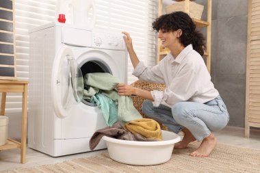 Çamaşır makinesinden çamaşırları çıkaran kadın.
