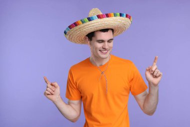 Meksika şapkalı genç adam menekşe arka plandaki bir şeyi işaret ediyor.