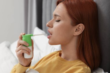 Genç kadın yatakta boğaz spreyi kullanıyor.