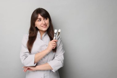 Gri arkaplanda kozmetik fırçaları olan kozmetik bilimci, metin için boşluk