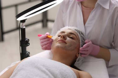 Kozmetik uzmanı klinikte kadının yüzüne maske takıyor.