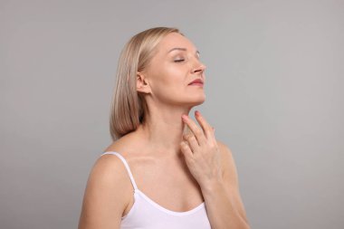 Gri arka planda güzel bir kadın boynuna dokunuyor.