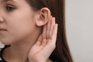 Gri arka planda işitme sorunu olan küçük bir kız, yakın plan. Metin için boşluk