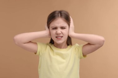 İşitme problemi. Soluk kahverengi arka planda kulak ağrısı çeken küçük bir kız.
