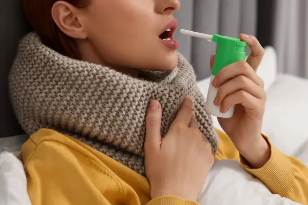 Young woman with scarf using throat spray in bed, closeup